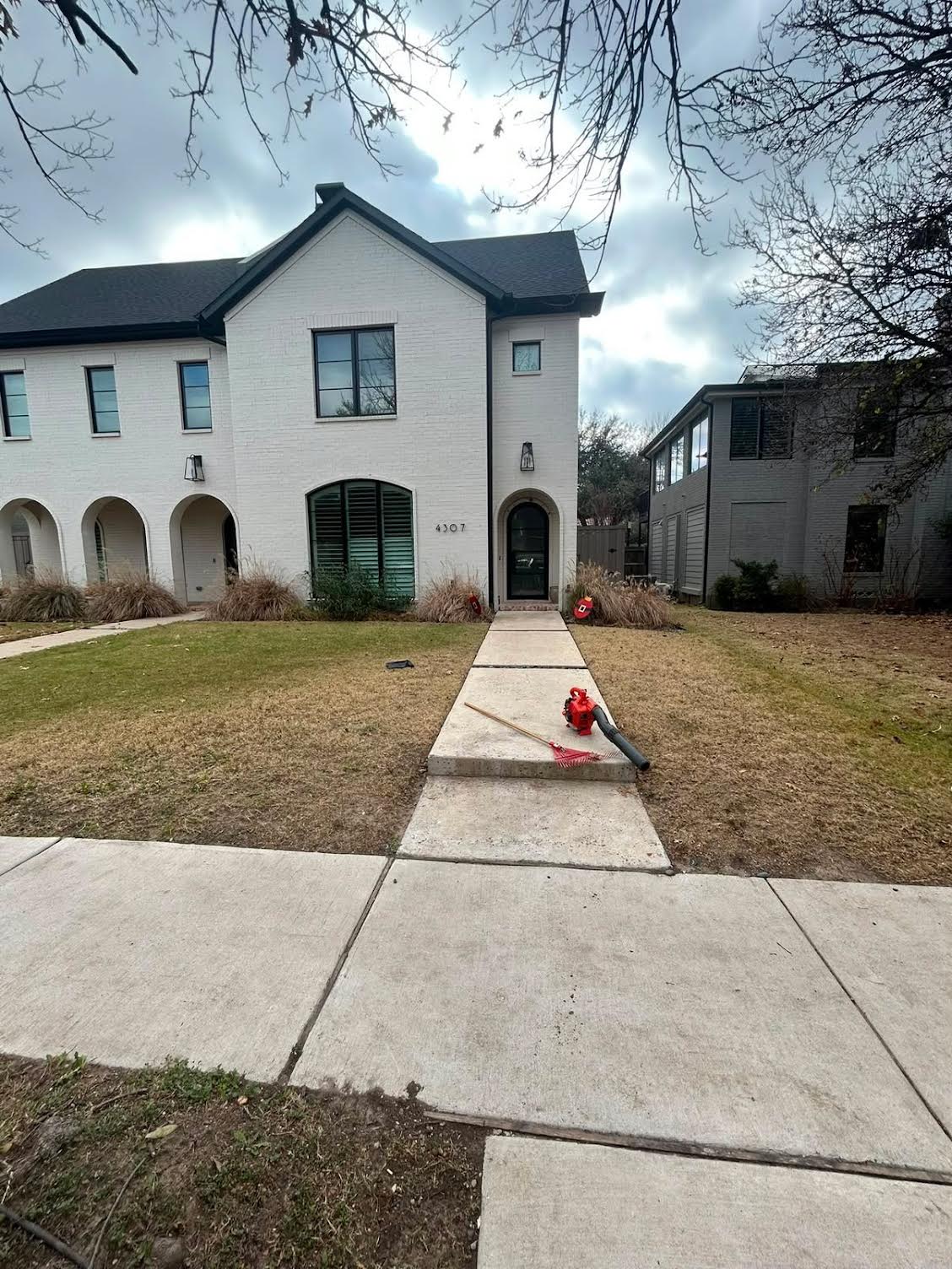 White brick townhome winter lawn cleanup with blower and rake on the walkway